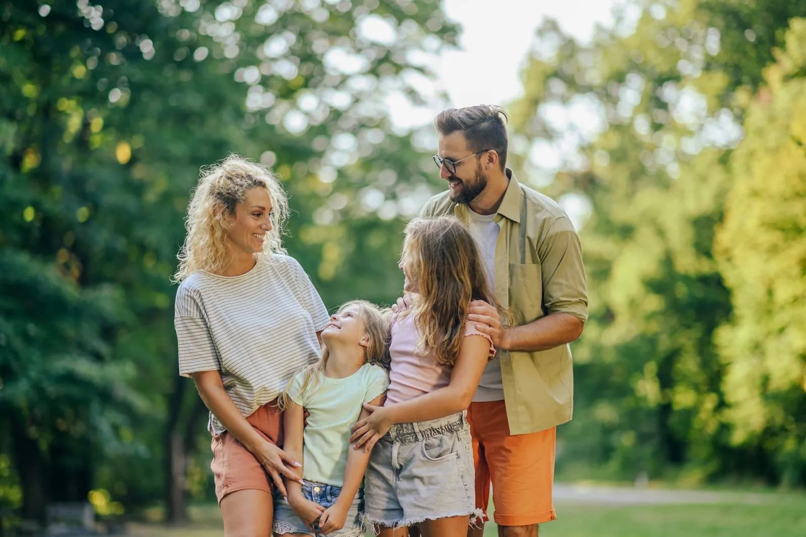 Padres sonriendo con sus dos hijas en un parque